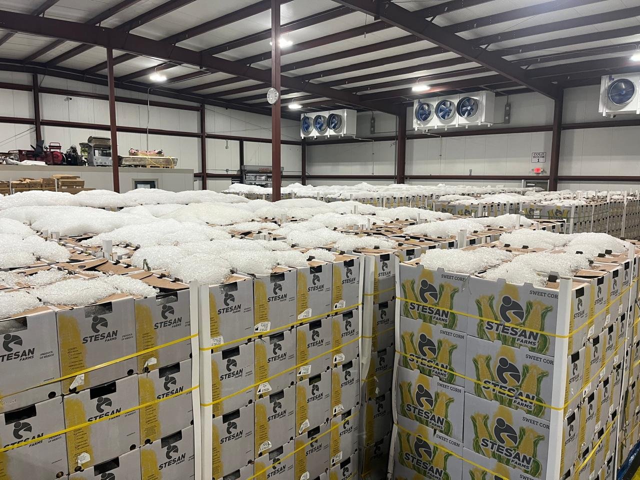 Large industrial warehouse filled with stacked yellow and white branded boxes and palletized goods under metal-beamed ceiling